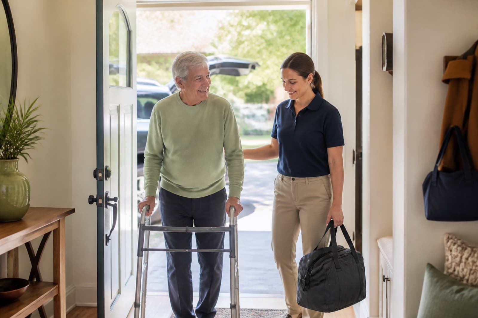 An older adult arriving home with a walker and professional support person
