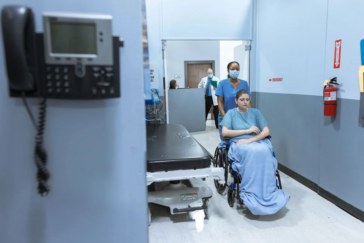 Nurse assisting a wheelchair patient in a hospital corridor