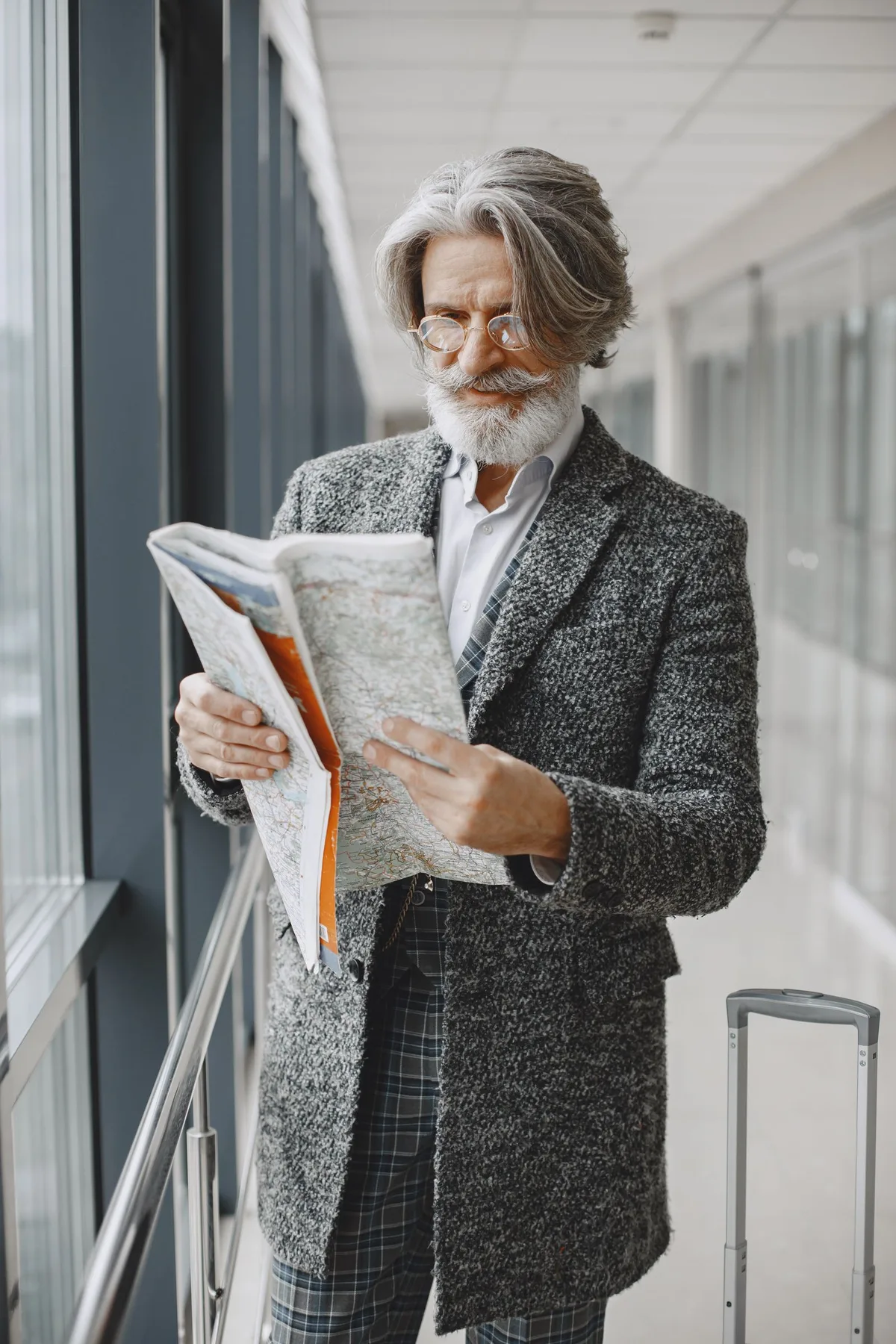 Older traveler with luggage reading a map in a terminal